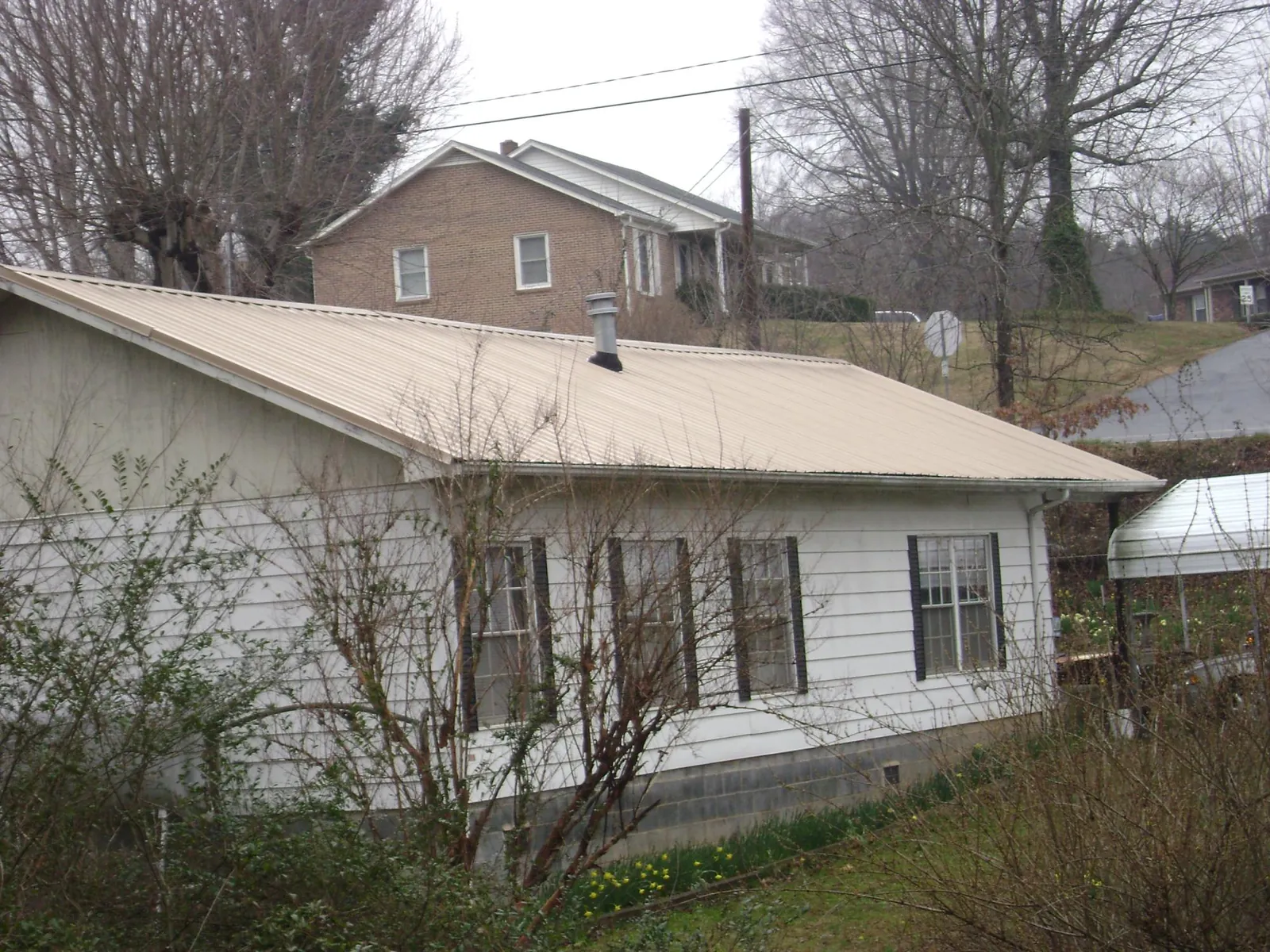 Tan metal roof on a white sided house set into a hillside — Commercial Roofing by Roofing Brothers in Martinsville